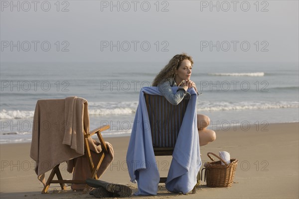 France, Pas-de-Calais, Escalles, Young women sitting on chair on empty beach. 
Photo : Jan Scherders