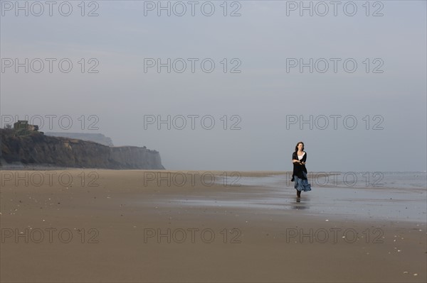 France, Pas-de-Calais, Escalles, Young woman strolling on empty beach. 
Photo : Jan Scherders