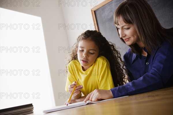 Schoolgirl writing with teacher in classroom. 
Photo : Rob Lewine
