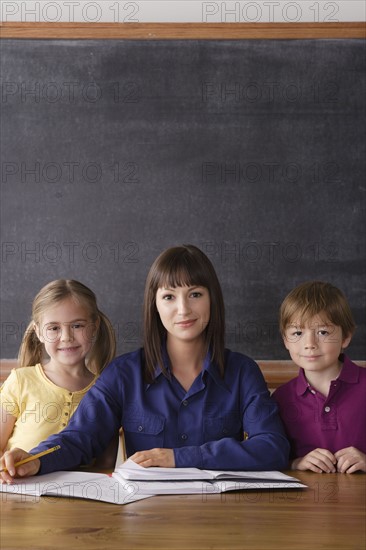 Teacher sitting by desk with two pupils. 
Photo : Rob Lewine