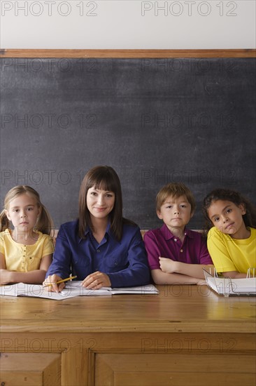 Teacher sitting by desk with group of pupils. 
Photo : Rob Lewine