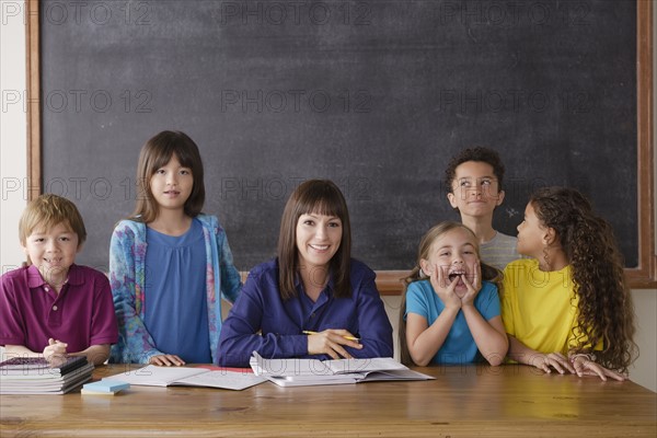 Teacher sitting by desk with group of pupils. 
Photo : Rob Lewine