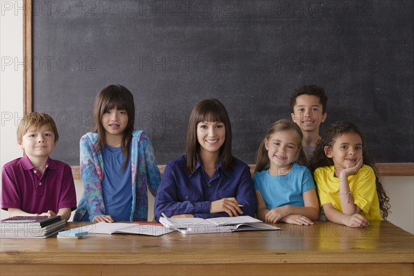 Teacher sitting by desk with group of pupils. 
Photo : Rob Lewine