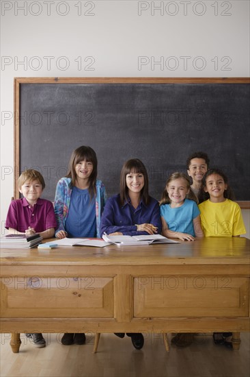 Teacher sitting by desk with group of pupils. 
Photo : Rob Lewine