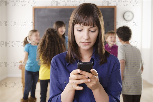 Teacher using mobile phone with group of pupils in background. 
Photo: Rob Lewine