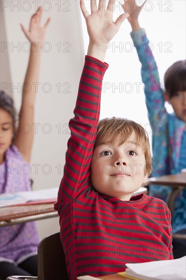 Pupils in classroom raising hands. 
Photo : Rob Lewine