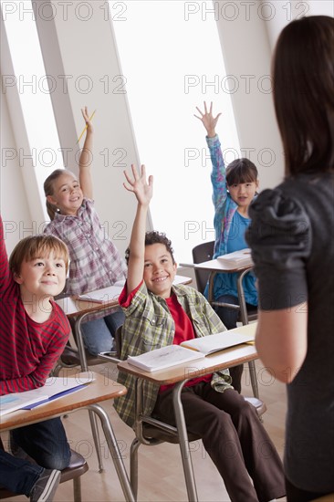 Pupils in classroom raising hands. 
Photo : Rob Lewine