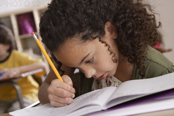 Close-up of writing girl (10-11) with boy (10-11) in background.
Photo : Rob Lewine