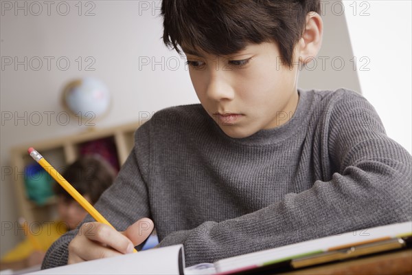 Writing boy (12-13) with boy (10-11) in background. 
Photo : Rob Lewine