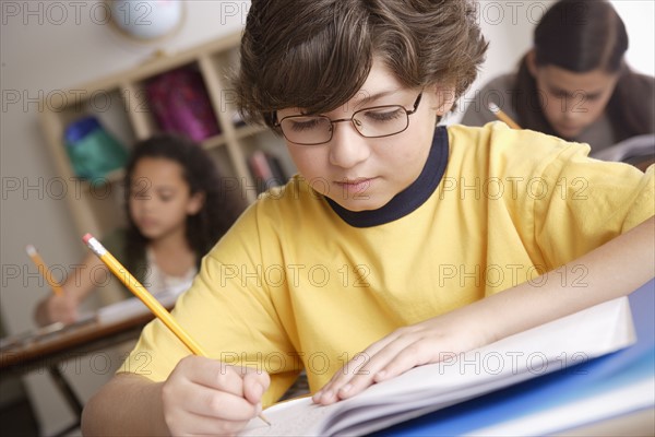 Writing boy (10-11) with girls (10-11, 12-13) in background. 
Photo : Rob Lewine