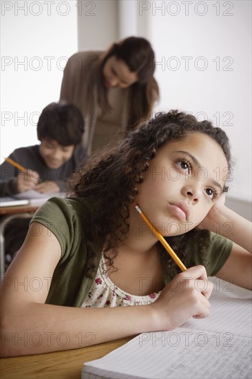 Schoolgirl (10-11) holding pencil with boy (12-13) and teacher in background. 
Photo : Rob Lewine