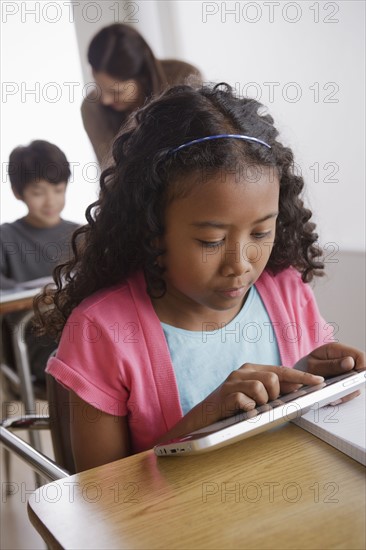 Schoolgirl (10-11) holding digital tablet with boy (12-13) and teacher in background. 
Photo: Rob Lewine