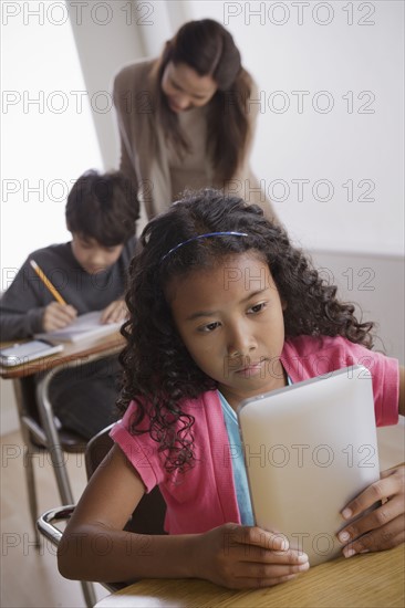 Schoolgirl (10-11) holding digital tablet with boy (12-13) and teacher in background. 
Photo : Rob Lewine