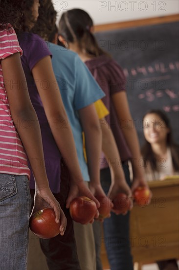 pupils standing in row (10-11, 12-13) holding apple with teacher in background. 
Photo : Rob Lewine