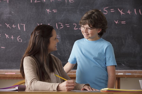 Schoolboy (10-11) and teacher face to face with blackboard in background. 
Photo : Rob Lewine