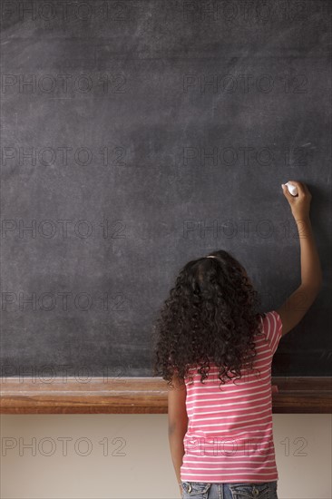 Portrait of schoolgirl (10-11) writing on blackboard. 
Photo : Rob Lewine