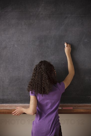Portrait of schoolgirl (10-11) writing on blackboard. 
Photo: Rob Lewine