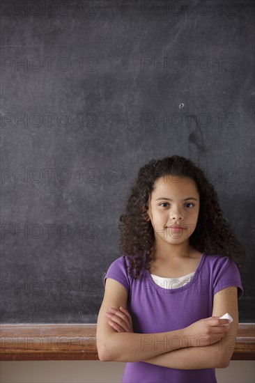 Portrait of schoolgirl (10-11) standing in front of blackboard. 
Photo : Rob Lewine