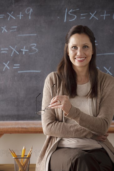 Portrait of teacher in classroom holding glasses. 
Photo: Rob Lewine