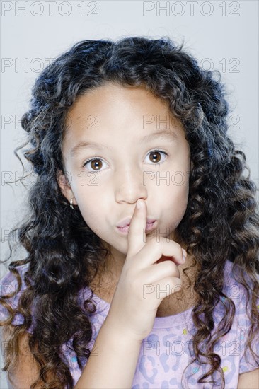 Portrait of girl (8-9) with finger on her lips, studio shot. 
Photo : Rob Lewine