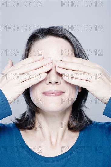 Smiling mid adult woman with hands covering eyes, studio shot. 
Photo : Rob Lewine
