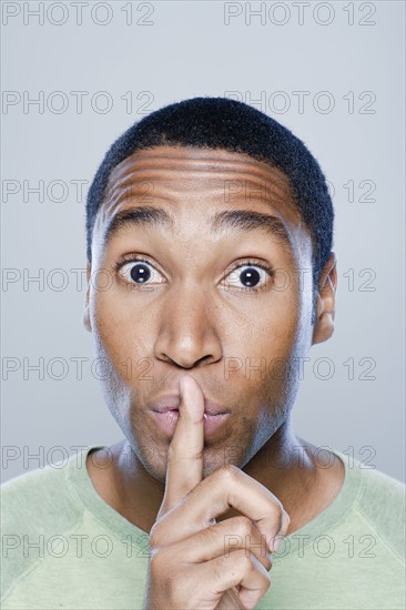 Portrait of young man with finger on his lips, studio shot. 
Photo: Rob Lewine