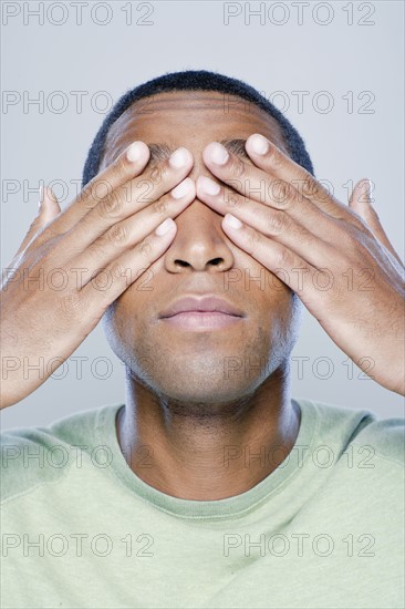 Young man with hands covering eyes, studio shot. 
Photo : Rob Lewine