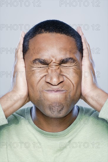 Young man with hands covering ears, studio shot. 
Photo: Rob Lewine