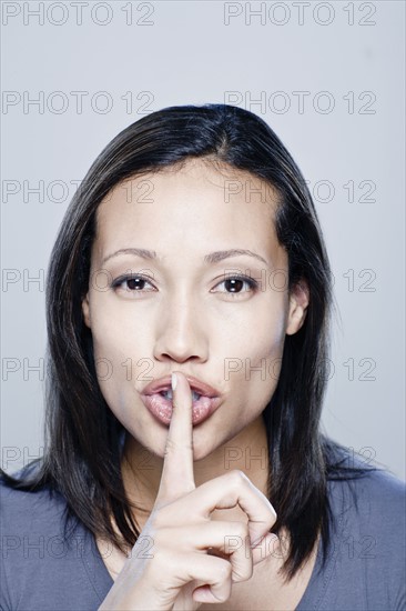 Portrait of young woman with finger on her lips, studio shot. 
Photo : Rob Lewine