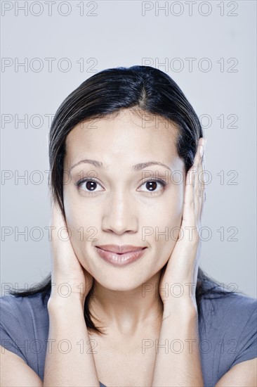 Portrait of young woman with hands covering ears, studio shot. 
Photo : Rob Lewine