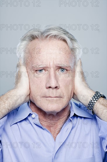 Portrait of senior man covering his ears, studio shot. 
Photo : Rob Lewine