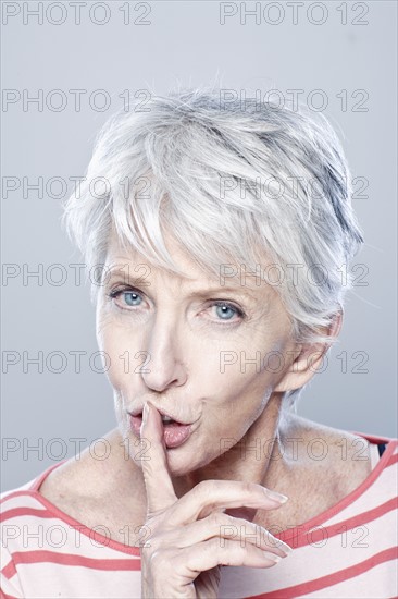 Portrait of senior woman with finger on her lips, studio shot. 
Photo : Rob Lewine