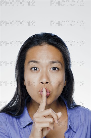 Portrait of young woman with finger on lips, studio shot. 
Photo : Rob Lewine