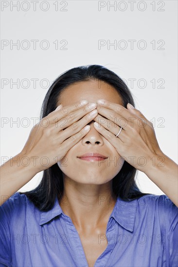 Portrait of young woman with hands covering eyes, studio shot. 
Photo : Rob Lewine