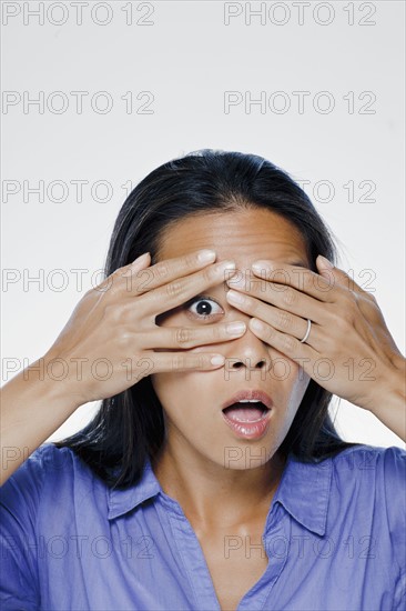 Portrait of young woman with hands covering eyes, studio shot. 
Photo : Rob Lewine