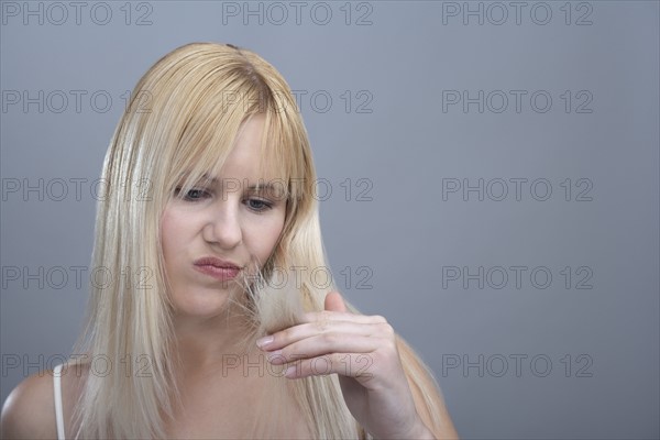 Woman looking disapprovingly at split ends, studio shot. 
Photo : Mark de Leeuw
