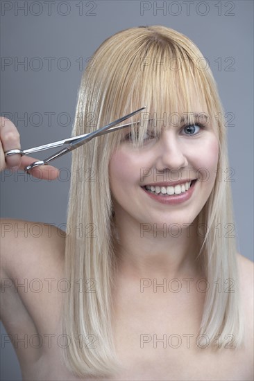 Woman cutting bangs, studio shot. 
Photo: Mark de Leeuw