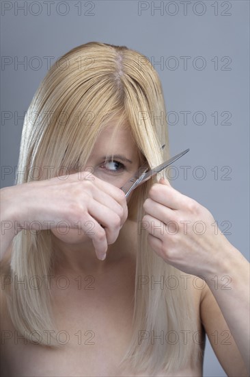 Woman cutting bangs, studio shot. 
Photo : Mark de Leeuw