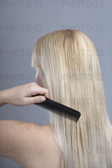 Woman combing hair, studio shot. 
Photo: Mark de Leeuw