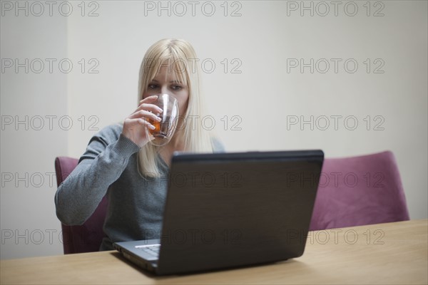 Netherlands, Goirle, Young woman relaxing in front of laptop and drinking tea. 
Photo : Mark de Leeuw