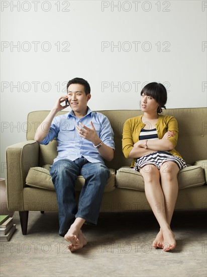 Young couple sitting on sofa, man talking via mobile. 
Photo : Jessica Peterson