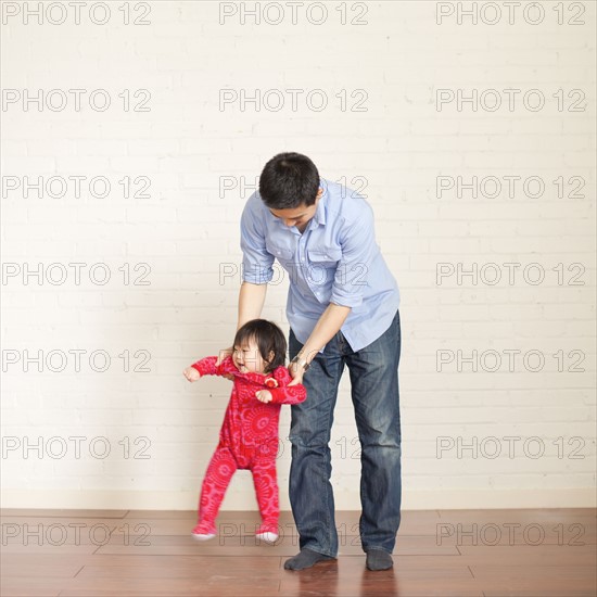 Father helping baby girl (12-17 months) with her first steps. 
Photo : Jessica Peterson
