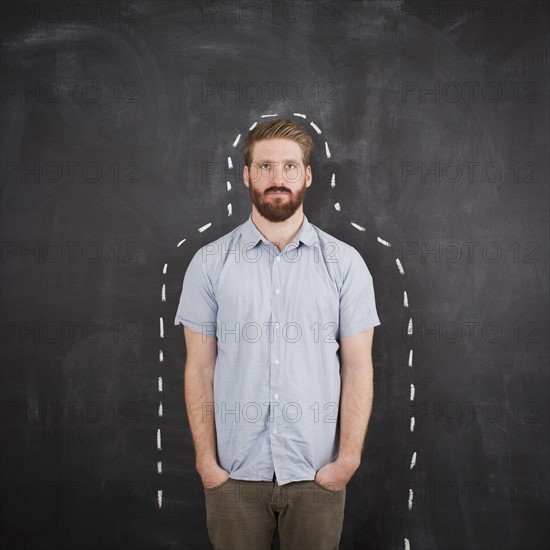 Young man with chalk outline on blackboard, studio shot. 
Photo : Jessica Peterson