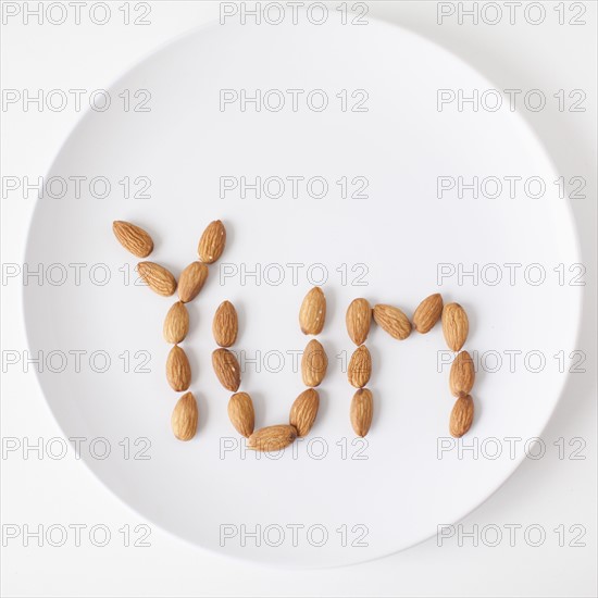 Word 'Yum' made out of almonds on plate, studio shot. 
Photo : Jessica Peterson