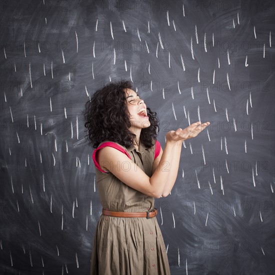 Young teacher posing against blackboard with V marks imitating rain.
Photo: Jessica Peterson