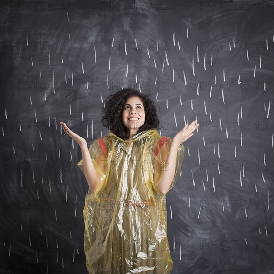 Young teacher wearing raincoat posing against blackboard with V marks imitating rain. 
Photo : Jessica Peterson