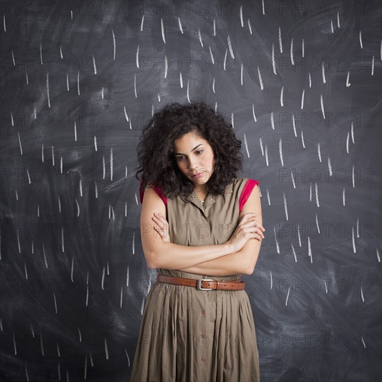 Young depressed teacher posing against blackboard with V marks imitating rain. 
Photo : Jessica Peterson