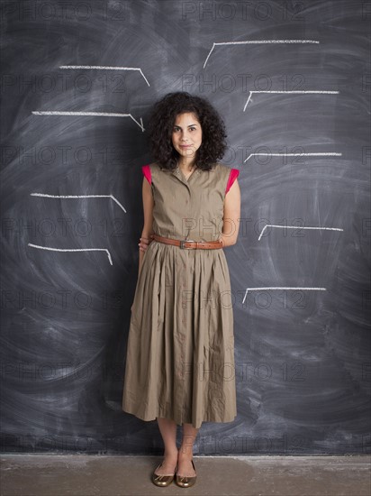 Young teacher posing against blackboard with blank lines written in chalk. 
Photo : Jessica Peterson
