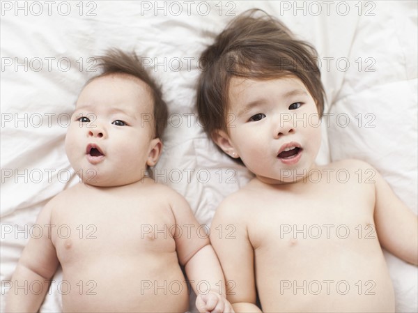 Mixed race siblings (2-5 months, 2-3) lying in bed side by side. 
Photo: Jessica Peterson