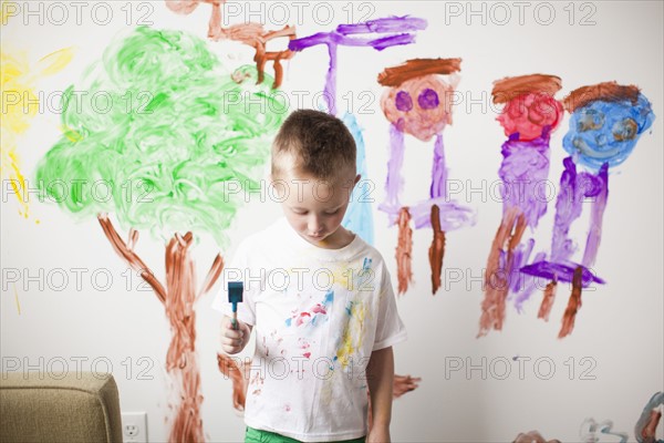 Toddler boy (2-3) standing in front of painted wall with guilt expression on his face. 
Photo : Jessica Peterson